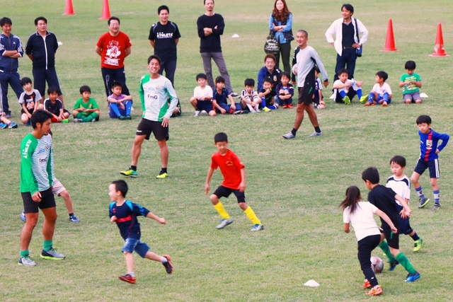 サッカーをしている子どもたちと指導をしているコーチ3人の様子の写真