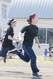 赤いはちまきをしている女子中学生と白いはちまきをしている女子中学生がコースを走っている様子の写真