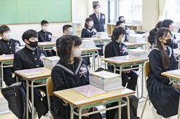 教室の椅子に座っている制服姿の新一年生たちの写真