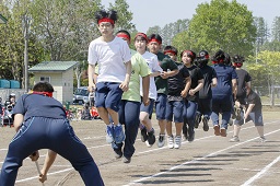 赤いはちまきをしている中学生たちが長縄跳びを飛んでいる瞬間の写真