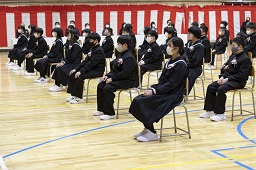 紅白幕が掛けられた会場で椅子に座っている新一年生たちの写真