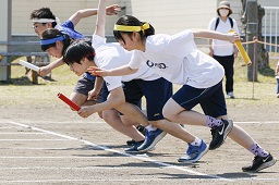 それぞれ白と青と赤と黄色のはちまきをした中学生4人がバトンを持って走り出す瞬間の写真