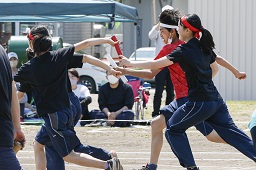 赤いはちまきをしている女子中学生と白いはちまきをしている男子中学生がそれぞれ次の走者にバトンを渡している瞬間の写真