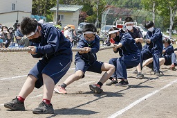 白いはちまきをしている中学生たちが全力で綱を引っ張っている写真