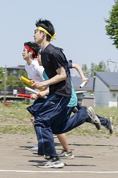 それぞれ赤や青や黄色のはちまきをした男子中学生がバトンを持って走っている写真