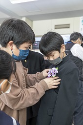 胸に紫色の花をさしてもらっている卒業生の写真