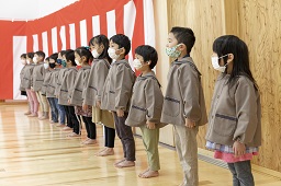 紅白幕が掛けられたホールで一列になって立っている児童たちの写真