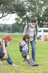 芝生の白線で女の子が履いているブーツが大きすぎて飛んでいないのを見守っている母親の写真