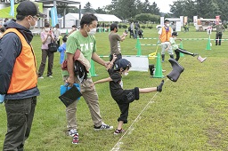 芝生の白線からお父さんに支えられながら男の子が履いているブーツを投げ飛ばしている瞬間の写真