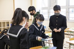 メッセージカードを読んでいる卒業生の女子とそれを囲むようにしている3人の卒業生の写真