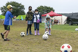 芝生の上に置いてある5個のサッカーボールを見ている4人の子どもたちの写真