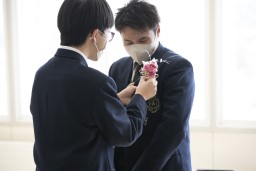 胸に桃色のバラを挿してもらっている卒業生の写真