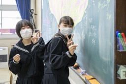 黒板への寄せ書きをしている途中でピースサインをしている卒業生の女子2人の写真