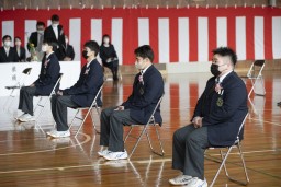 紅白幕が掛けられた体育館でパイプ椅子に座っている4人の卒業生たちの写真