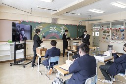 黒板に祝卒業と書かれている教室で座っている卒寮生たちの写真