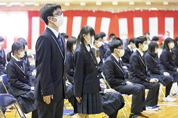 紅白幕が掛けられた会場で椅子に座っている新一年生たちと起立している男女2人の新一年生の写真
