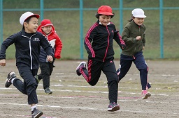 それぞれ赤い帽子や白い帽子をかぶっている4人の小学生がグラウンドで競走している写真