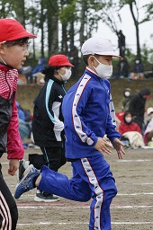 白い帽子をかぶった小学生と赤い帽子をかぶった2人の小学生がグラウンドで走っている写真