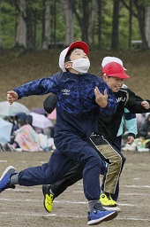 白い帽子をかぶった2人と赤い帽子をかぶった小学生がグラウンドで走っている写真