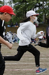 グラウンドで赤い帽子の小学生より先を走っている白い帽子の小学生の様子の写真