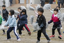 銀色のボンボンを両手に持ってグラウンドで踊っている小学生たちの写真