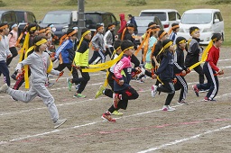 グラウンドを走っている黄色い長めのはちまきを巻いた小学生たちの写真