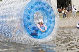 巨大なビニールでできた筒が水面に浮いていて中から女の子が顔を出している様子の写真
