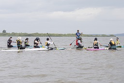 水面で人利用ボードの上に座っている10人の参加者とボードに立ち上がっているスタッフの写真