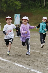 白い帽子の3人の小学生たちがグラウンドを走っている様子の写真