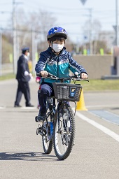 自転車に乗ってコースを走っている青いヘルメットをかぶった小学生の写真