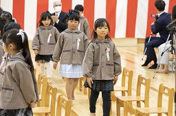 紅白幕が掛けられた会場に入場してくる卒園児たちの写真