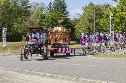 赤いトラクターと金色の神輿と祭りの参加者たちの様子の写真