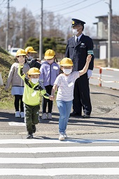 小学生たちが2人1組で手をつなぎながら手を上げて横断歩道を歩いている小学生の写真