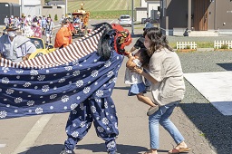 青い獅子舞の顔にに子どもを差し出している母親の写真