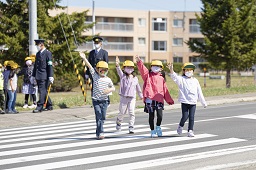 小学生4人が右手を上げて横断歩道を歩いている様子の写真