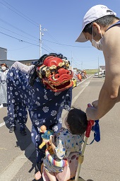 ベビーカーに乗っている子どもとその目の前に立つ青い獅子舞の写真