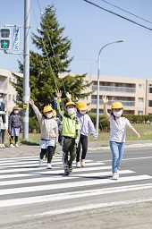 小学生4人が右手を上げて横断歩道を歩いている様子の写真その2