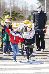 小学生たちが2人1組で手をつなぎながら手を上げて横断歩道を歩いている小学生の写真その2