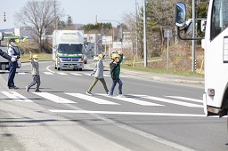 右手を上げて横断歩道を渡っている小学生3人の写真