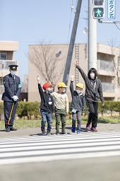 横断歩道を右手を上げて渡ろうとしている小学生3人と先生の様子の写真