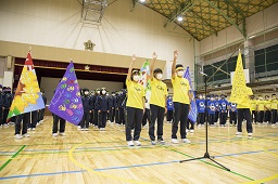 体育館で黄色のシャツを着た3人の中学生が生徒一同の前で右手を上げて選手宣誓をしている写真