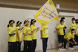 黄色いシャツと黄色いはちまき姿の中学生たちが体育館で黄色い旗を持って応援している写真