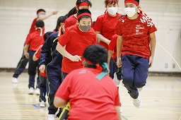 赤いシャツと赤いはちまきを付けた中学生たちが長縄跳びに挑んでいる様子の写真