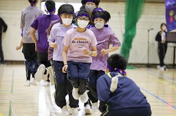 紫色のシャツとはちまきを着けた中学生たちが体育館で長縄跳びに挑んでいる様子の写真