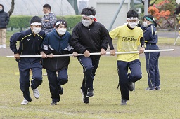 白いはちまきをした4人の中学生が横一列に並んで白い棒を持ってグラウンドを走っている写真