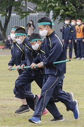 緑のはちまきをした4人の中学生が横一列に並んで緑の棒を持ってグラウンドを走っている写真その2