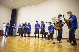 ステージ上でギターを演奏している生徒と数名の生徒が歌っている写真