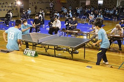 ステージ上で卓球で試合をしている生徒と観戦している生徒たちの写真