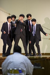 ステージ上でスーツにネクタイ姿の男子高校生5人がパフォーマンスを披露している写真