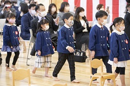 紅白幕が掛けられた会場に入場してくる卒園児たちの写真その1